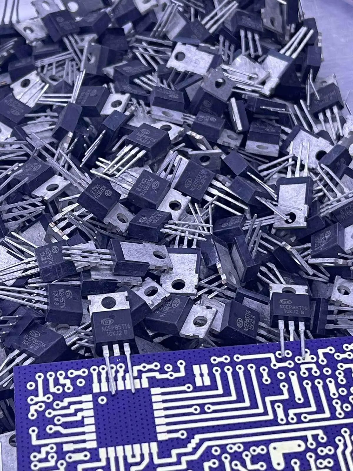 Pile of black NCEP85T16 electronic components with metal pins and a blue circuit board