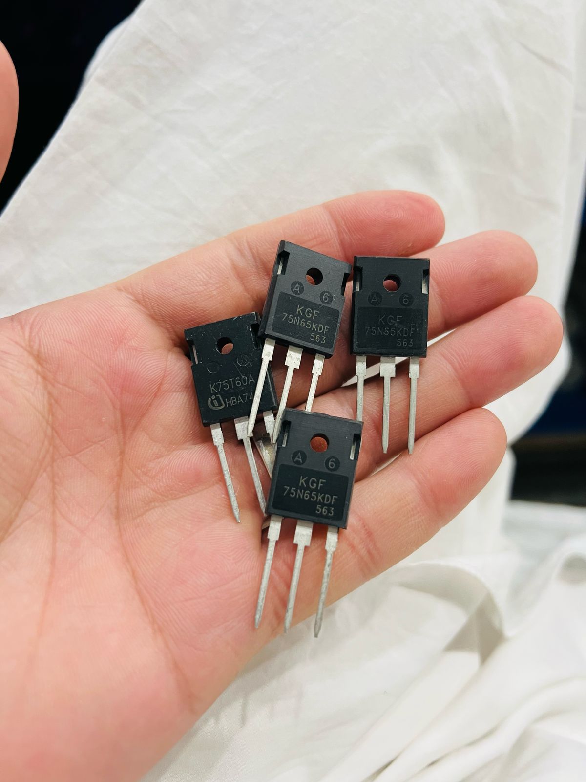 Hand holding four RN75H65 electronic components from The Component Centre with three metal pins each