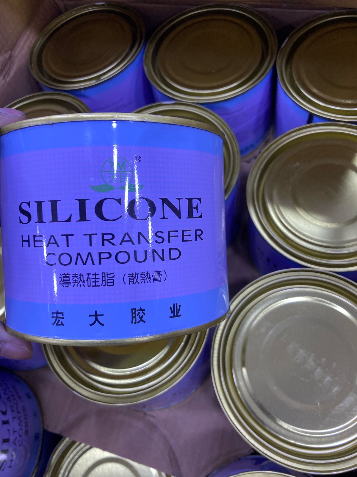 Blue can of Silicone Thermal Paste 750G heat transfer compound held above similar cans