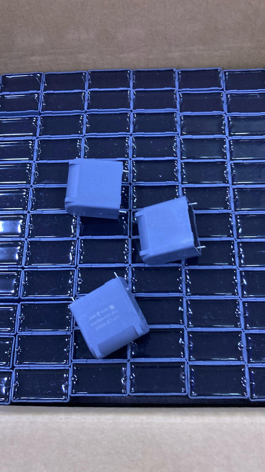 Three 12uF 600V blue capacitors placed on a black grid surface inside a box