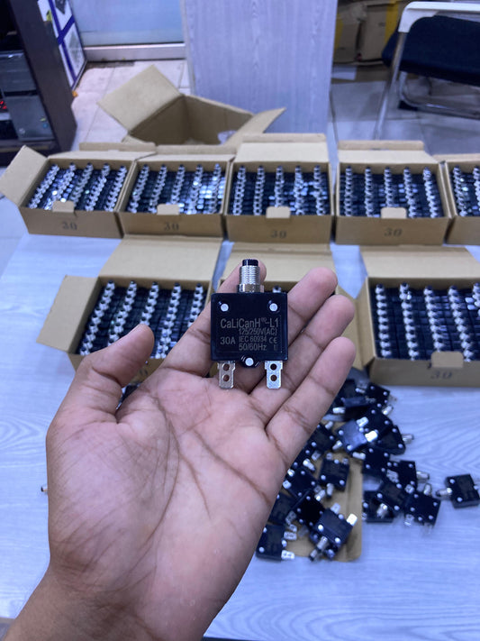 Hand holding Calicanh-L1 125/250V thermal circuit breaker with packed boxes of units behind