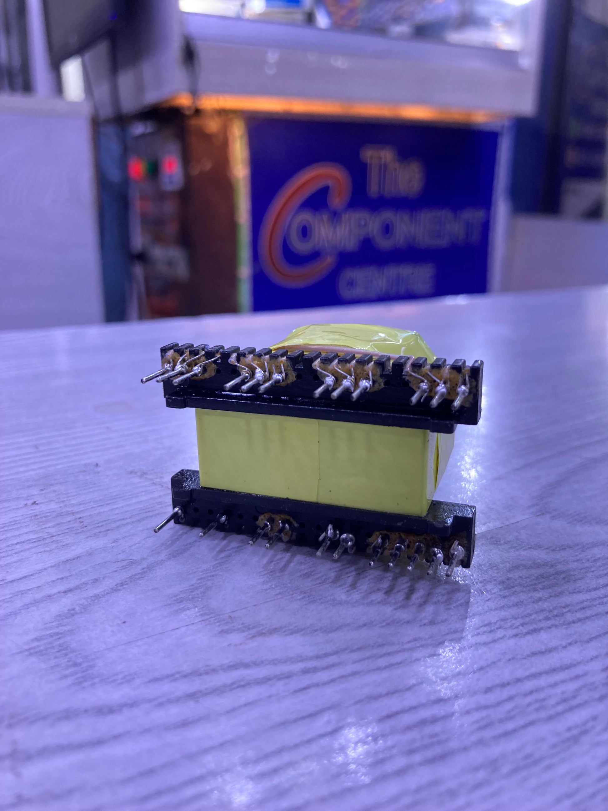 EE33-1.5-15KW transformer component with 23 metal pins from The Component Centre on a wooden surface