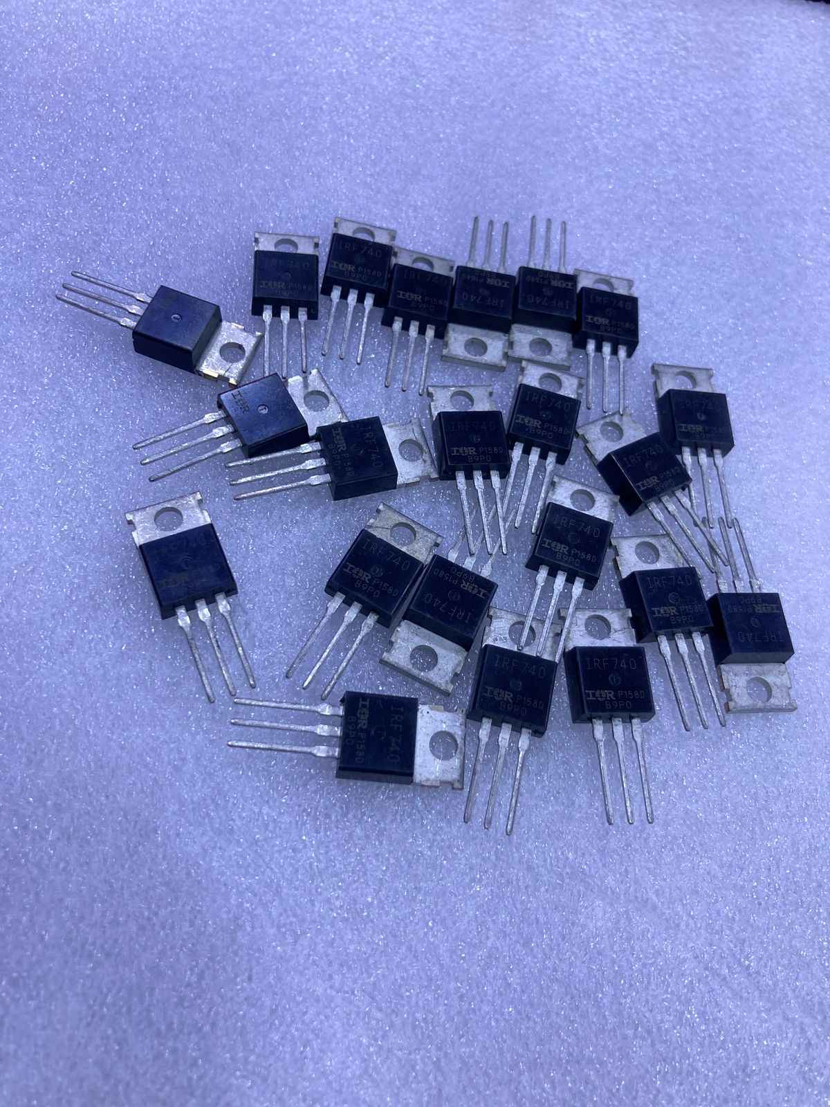 Multiple IRF740 electronic transistors with three pins and metal tabs on a soft surface