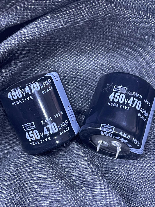 Two black 470uF 450V Capacitor electronic components with labeled polarity resting on gray fabric
