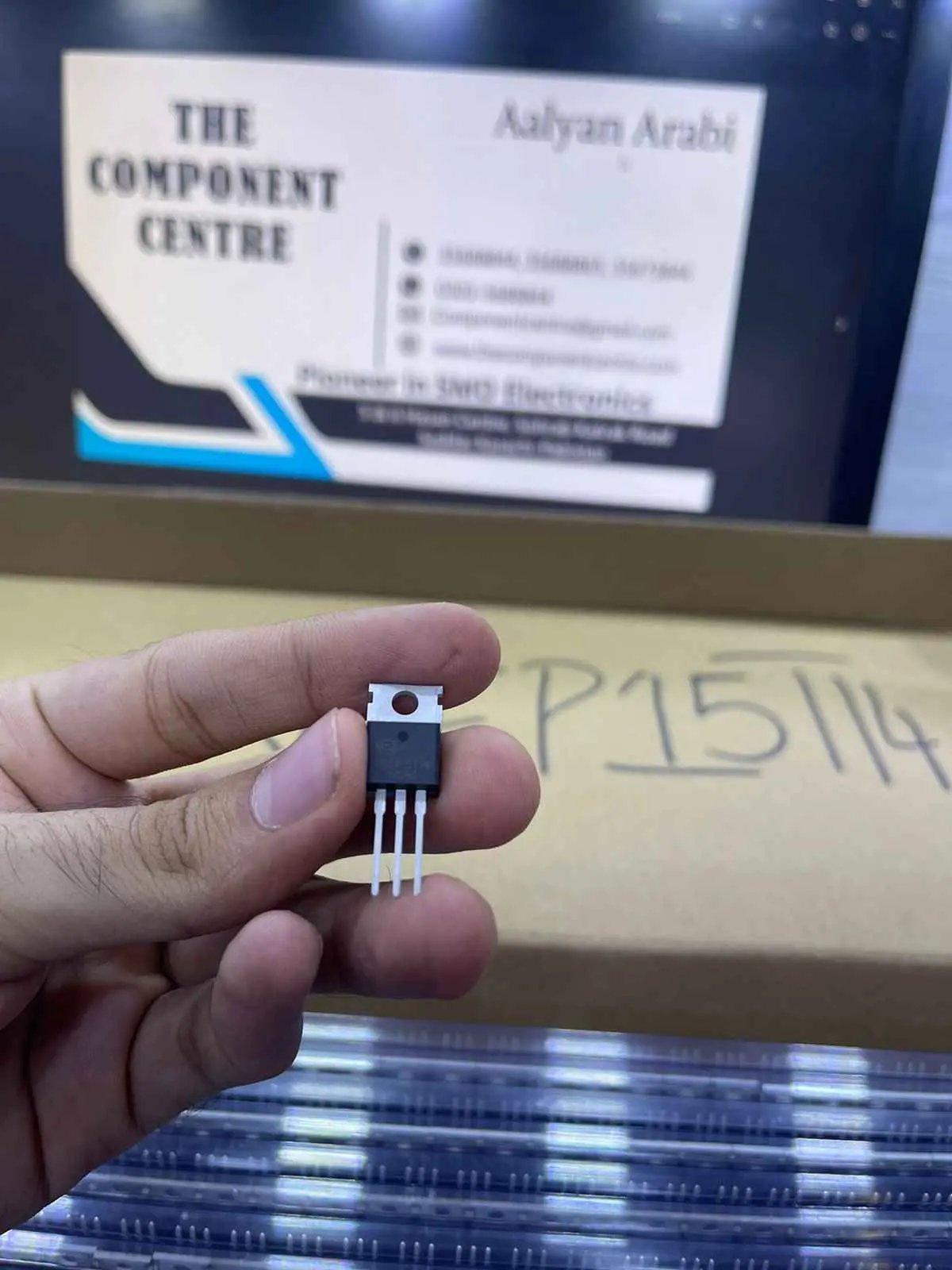 Close-up of hand holding NCEP15T14 transistor component with The Component Centre label in background