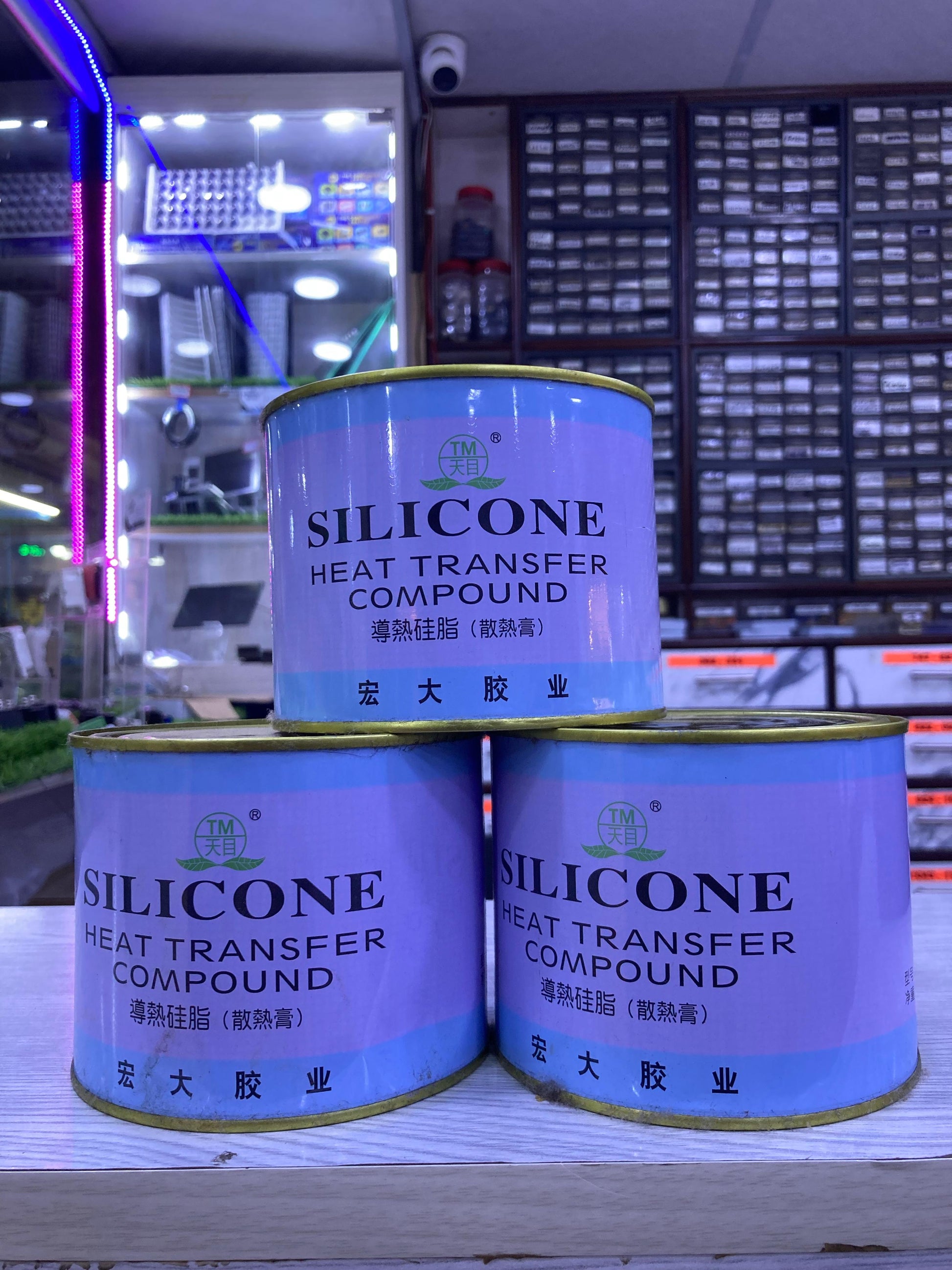 Three cans of Silicone Thermal Paste 750G heat transfer compound stacked in an electronics store