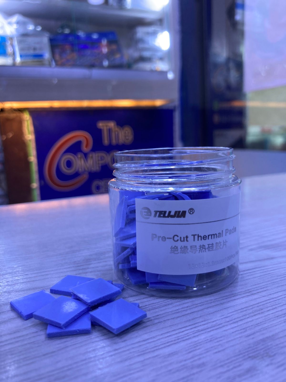 Jar of blue Pre-Cut Thermal Silicone Pads on a table with several pads displayed and The Component Centre sign in background
